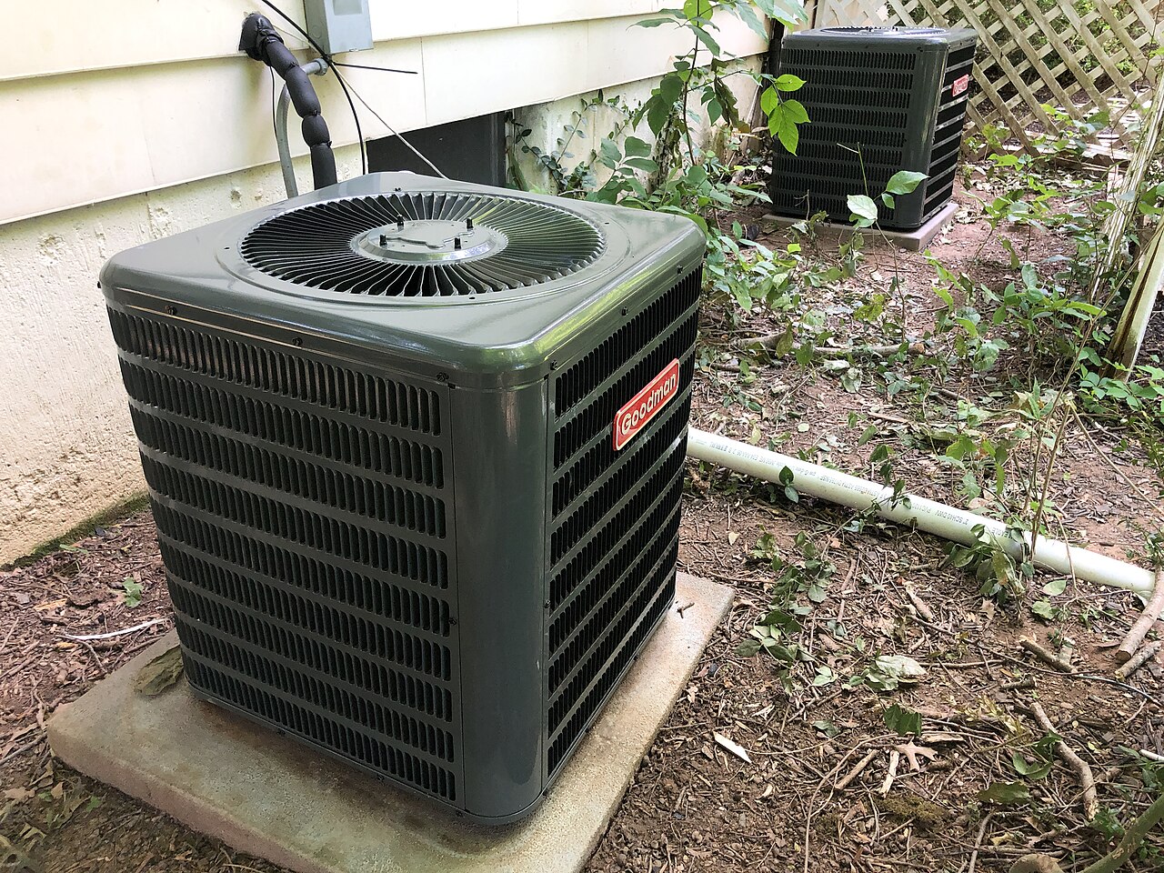 Central air conditioner condenser unit sitting on a concrete pad beside a house